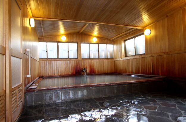 “Sukayu Onsen women’s indoor bath — a wooden hot spring room with soft lighting and natural geothermal water (official photo).”