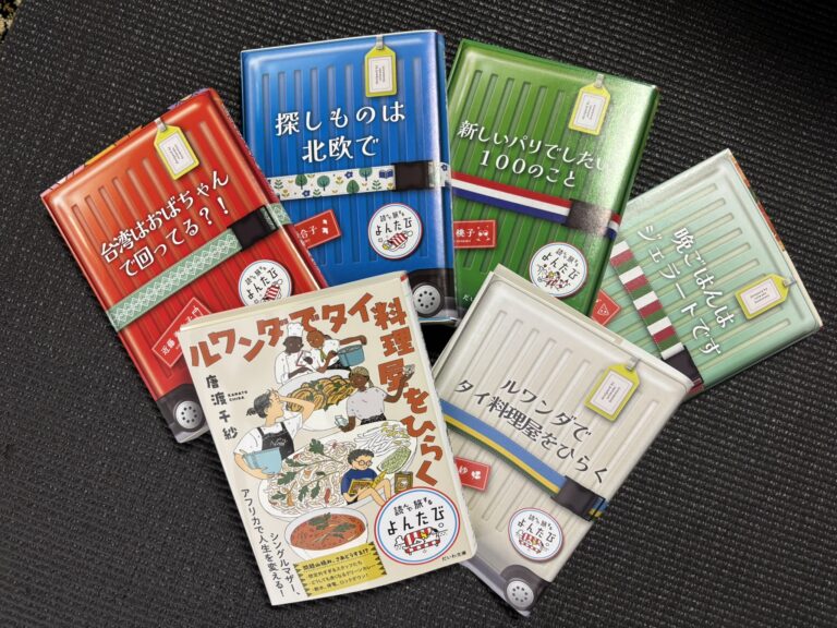 Five Japanese paperback books with colorful suitcase-themed covers from the “Travel by Reading” series.