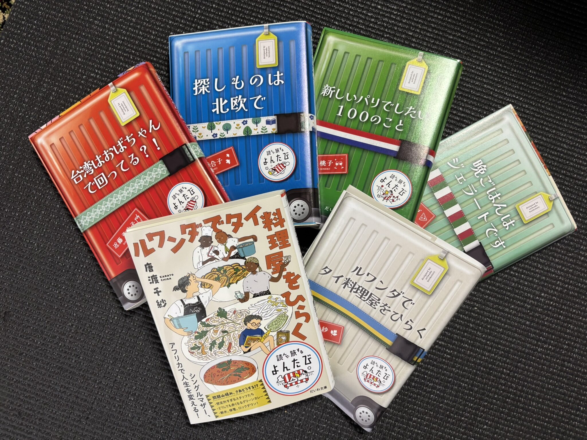 Five Japanese paperback books with colorful suitcase-themed covers from the “Travel by Reading” series.