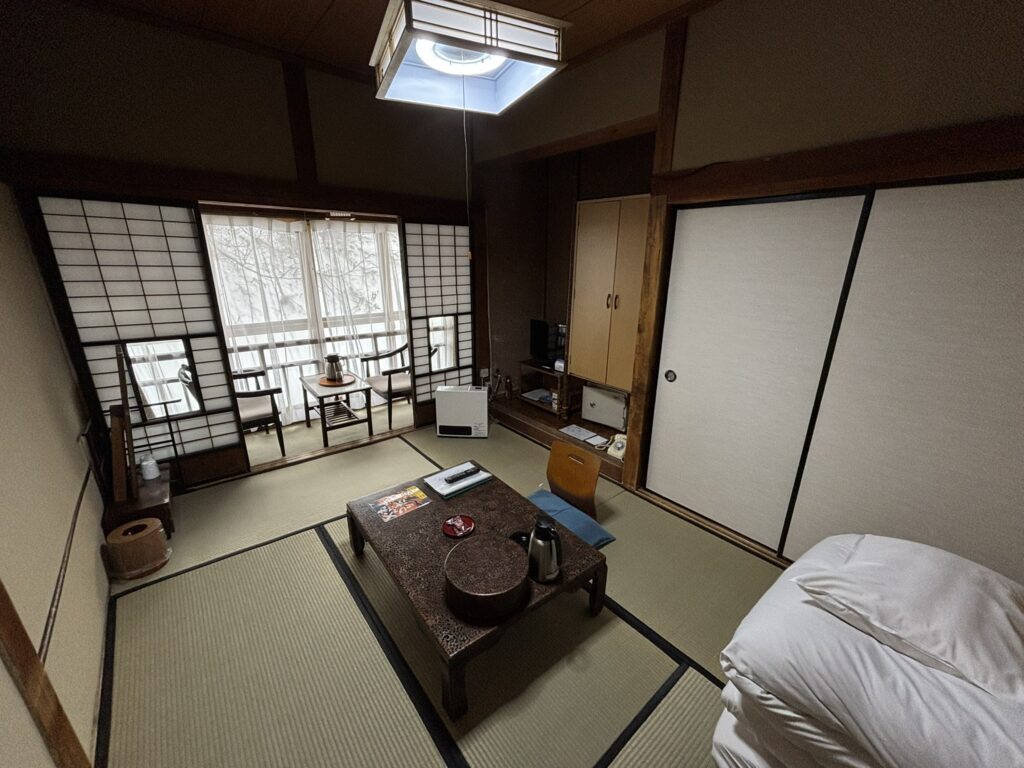 A traditional tatami room at Sukayu Onsen with fusuma sliding doors, a futon, a cord-pull ceiling light, and a snowy view from the window.
