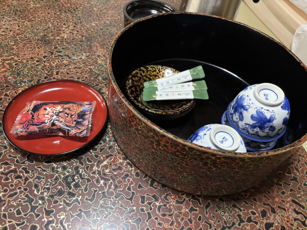 Tea, a Nebuta-themed sweet, teacups, and Tsugaru-nuri lacquerware on a table in a room at Sukayu Onsen.